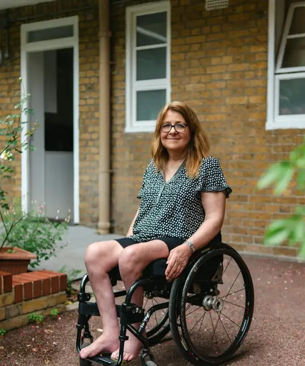 A smiling woman in a wheelchair outside the front door of her home