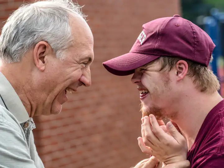 A young man with Down syndrome laughing with an older family member